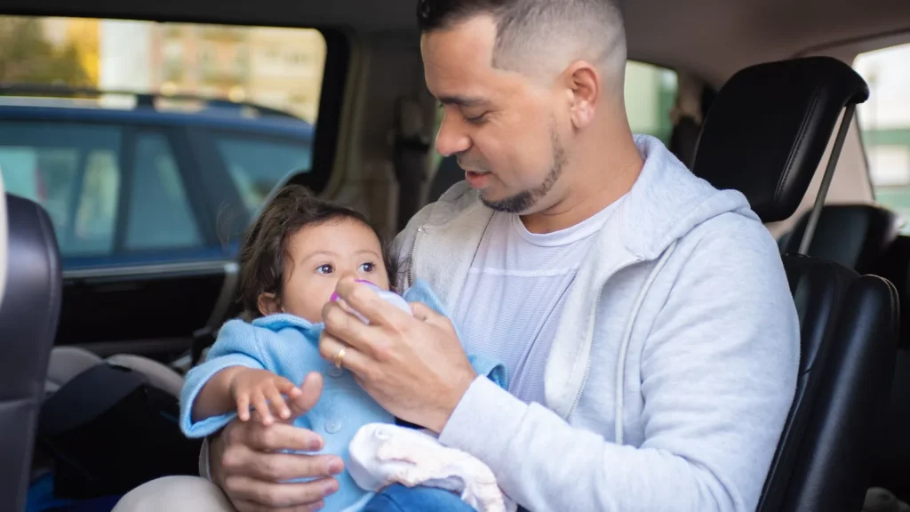 Un padre da el biberón a su bebé dentro de un coche, antes de un trayecto con silla infantil en un taxi de La Meca