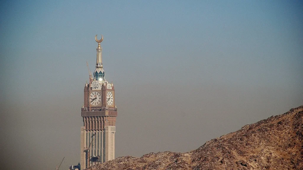 La Torre del Reloj de La Meca se alza sobre colinas rocosas con la luz brumosa de primera hora, ideal para una ziyarah por la mañana en La Meca