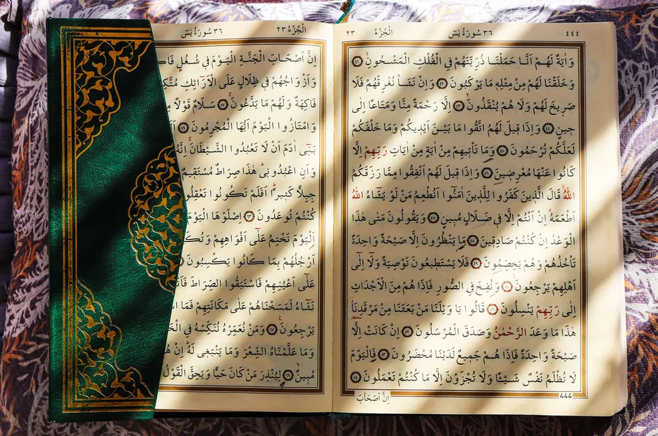 Aufgeschlagener Koran mit grün-goldenem Einband auf gemustertem Stoff im Sonnenlicht, Symbolbild zum Koran-Museum in Mekka