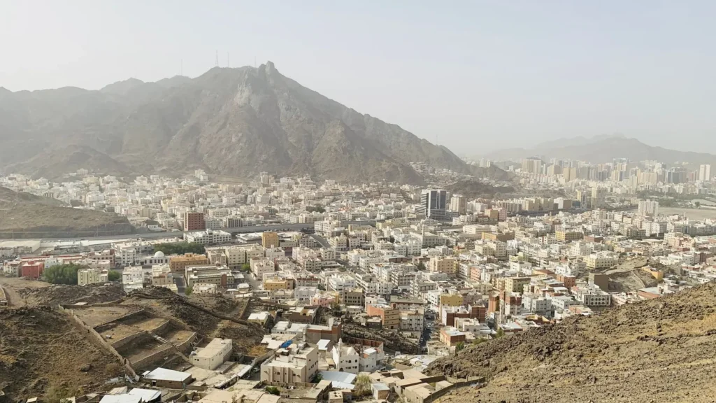 Barrios de la ciudad extendidos por un valle bajo una montaña rocosa en un día brumoso, el paisaje de La Meca que recorre un taxi a Jabal Thawr