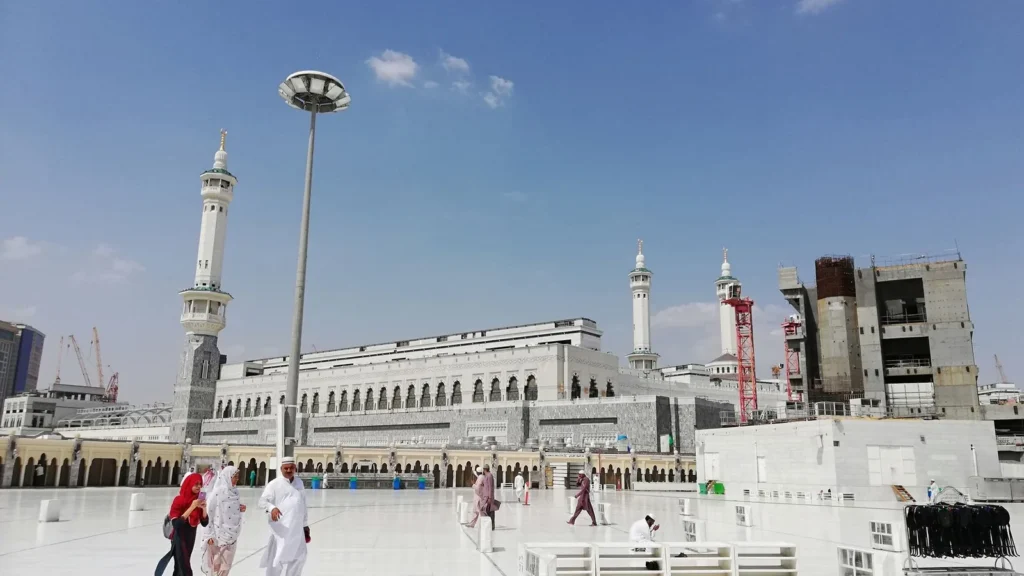 Pilgrims in white walking across the open marble square beside the Grand Mosque in Makkah