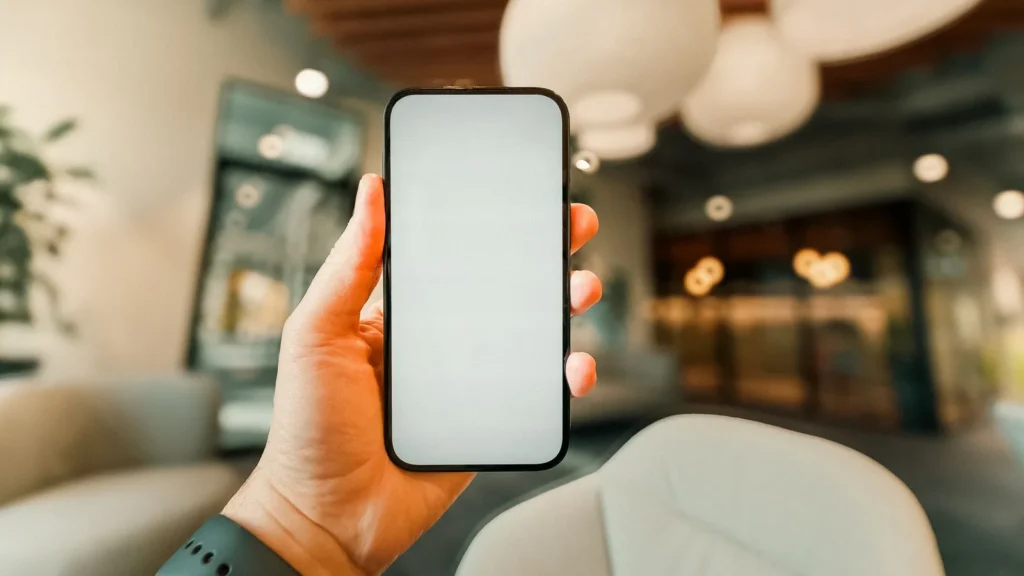 Mano che tiene uno smartphone con lo schermo vuoto nella hall di un hotel, mentre si consulta il preventivo di un taxi alla Mecca