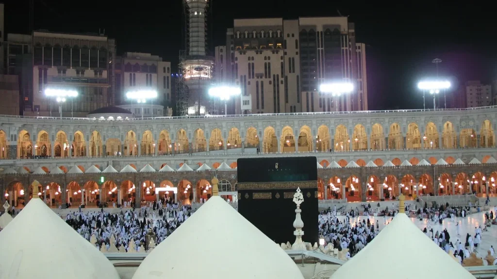 Die beleuchtete Heilige Moschee in Mekka bei Nacht mit Pilgern rund um die Kaaba, Ausgangspunkt für einen Besuch der Masjid Aisha bei Nacht