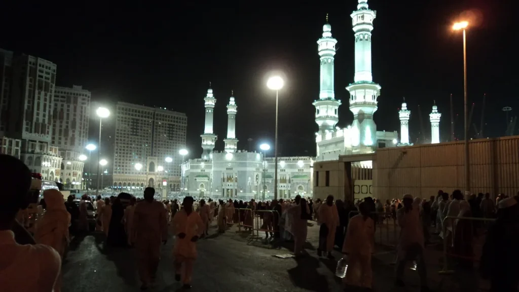 Beleuchtete Minarette der Heiligen Moschee in Mekka bei Nacht mit Gläubigen davor – wo ist Masjid Aisha von hier aus