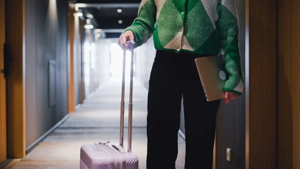 Viajero caminando por el pasillo de un hotel con una maleta y un portátil, preparado para una ziyarah el último día en La Meca