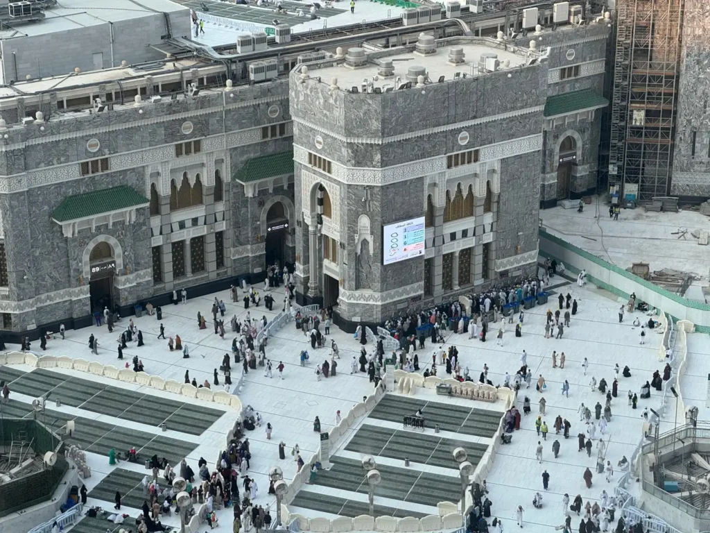 Menschen vor nummerierten Eingängen der Heiligen Moschee in Mekka; die Karte der Heiligen Moschee verzeichnet diese Tore